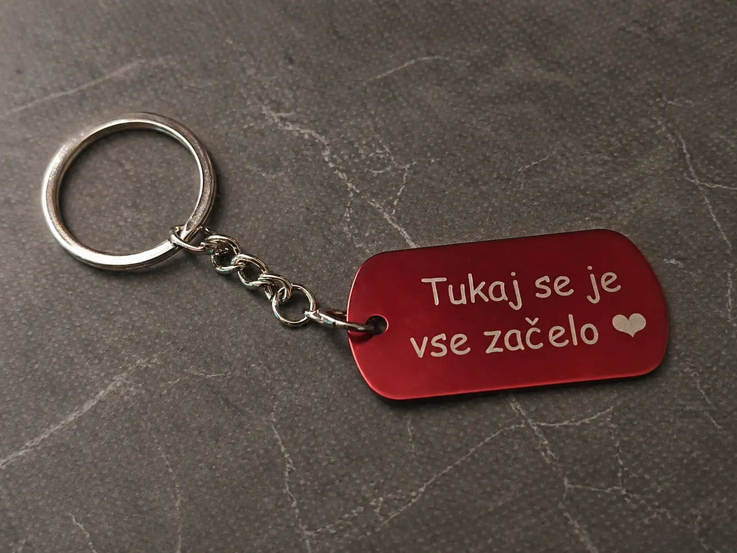 Personaliziran kovinski obesek za ključe z gravuro na minimalističnem sivem ozadju