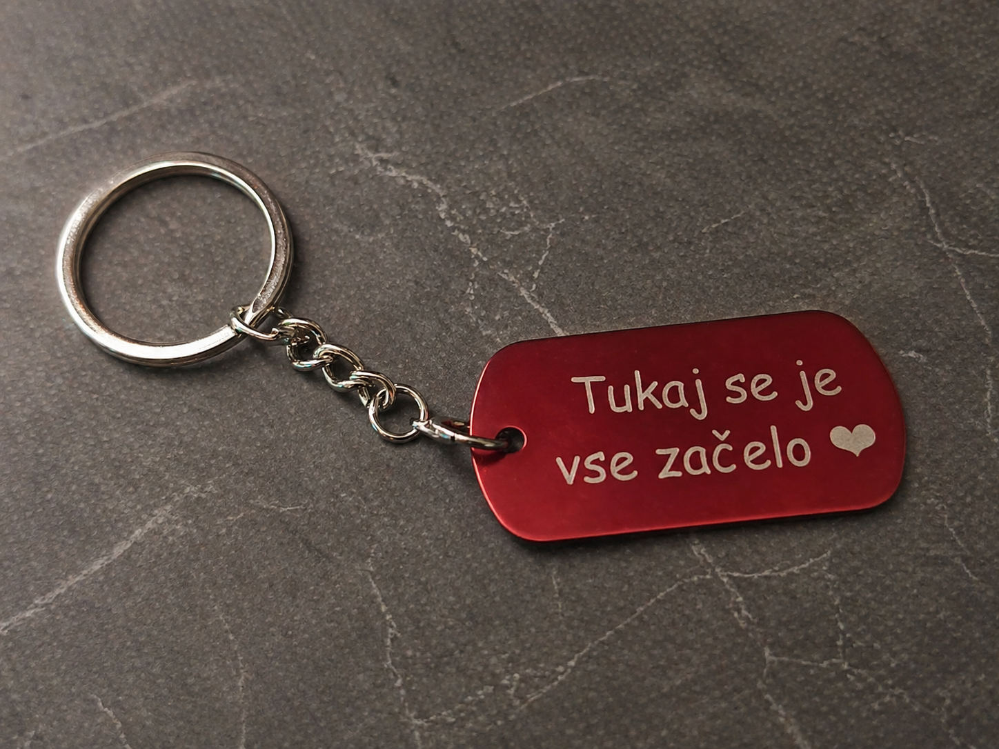 Personaliziran kovinski obesek za ključe z gravuro na minimalističnem sivem ozadju